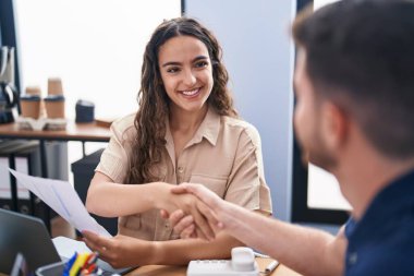 Young hispanic couple business workers shake hands at office