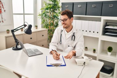 Doktor üniforması giyen İspanyol genç adam klinikteki belgeye yazı yazıyor.