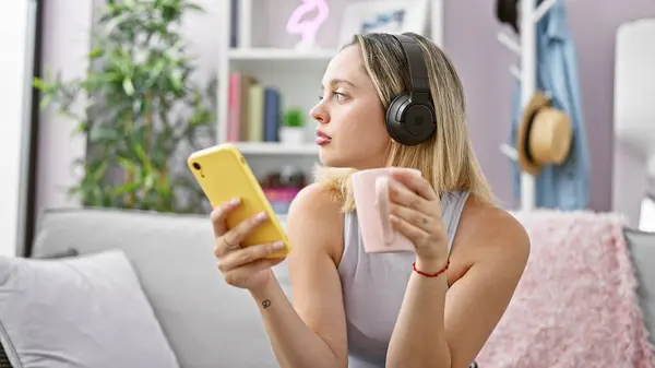 Mujer Rubia Joven Usando Smartphone Auriculares Bebiendo Café Casa —  Fotos de Stock