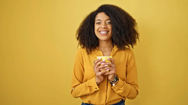 非洲裔美国妇女站在孤立的黄色背景上喝咖啡 — 图库照片