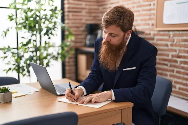 Young redhead man business worker using laptop writing on notebook at office