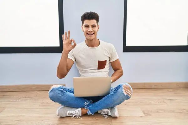 自宅でラップトップを使用している若いヒスパニックの男性は 手と指でOkサインを行い ポジティブに微笑んでいます 成功した表現 — ストック写真