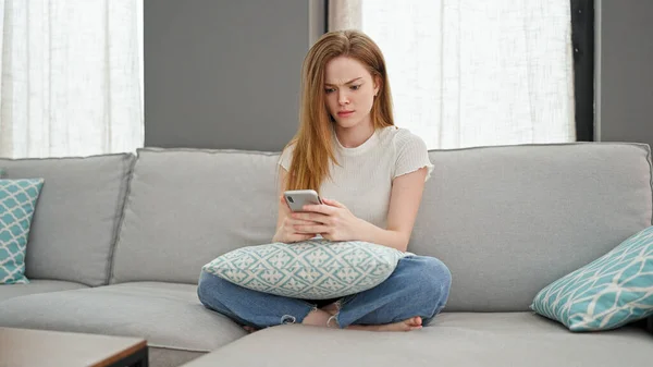 自宅で動揺しているスマートフォンを使用して金髪の若い女性 — ストック写真