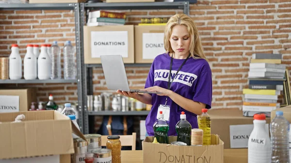 Young Blonde Woman Volunteer Checking Products Using Laptop Charity Center — Stock Photo, Image