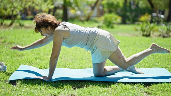 Middle age woman stretching back on yoga mat at park