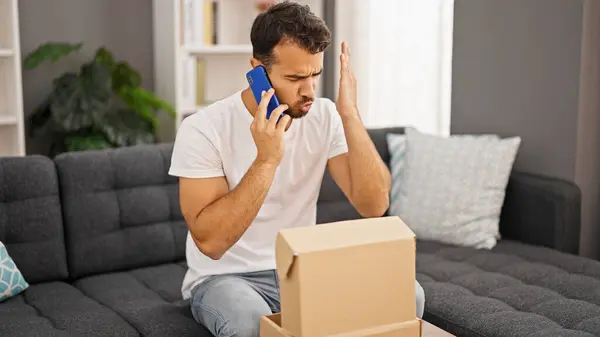 Young Hispanic Man Angry Speaking Phone Unpacking Cardboard Box Home — Stock Photo, Image