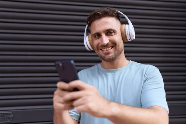Young hispanic man listening to music over isolated black metal background