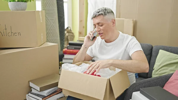 Young Caucasian Man Unpacking Cardboard Box Talking Smartphone New Home — Stock Photo, Image