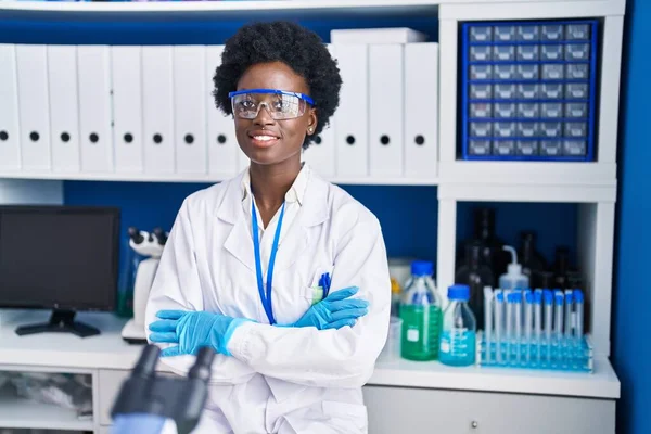Young african american woman scientist standing with arms crossed gesture at laboratory