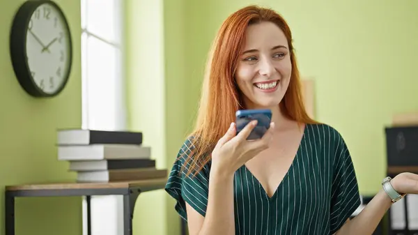 年轻的红头发女商人通过在办公室工作的智能手机发送语音讯息 — 图库照片