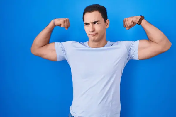 Ung Latinamerikansk Man Står Över Blå Bakgrund Visar Armar Muskler — Stockfoto