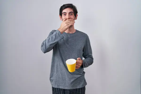 Молодой Латиноамериканец Пижаме Пьющий Чашку Кофе Шоке Закрывая Рот Руками — стоковое фото