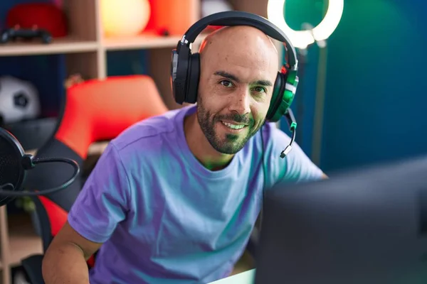 Young bald man streamer playing video game using computer at gaming room