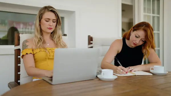 ノートパソコンを使っている2人の女性が自宅のテラスのテーブルに座って — ストック写真