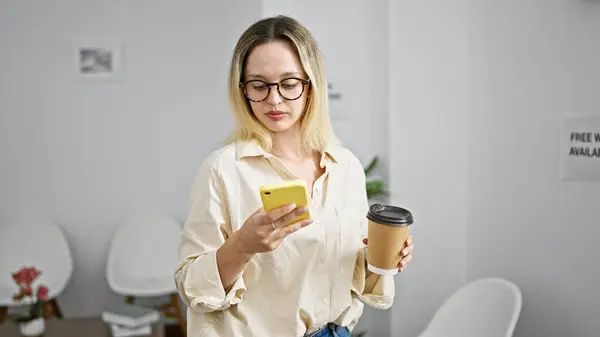 Young blonde woman business worker using smartphone drinking coffee at the office