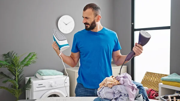 Young hispanic man choosing ironing machine at laundry room