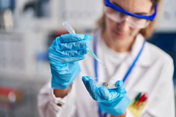 Young woman scientist pouring liquid on sample at laboratory