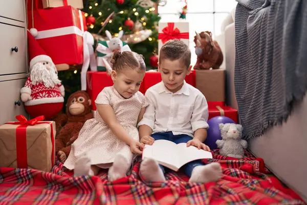 Двое Детей Читают Книгу Сидя Полу Елки Дома — стоковое фото