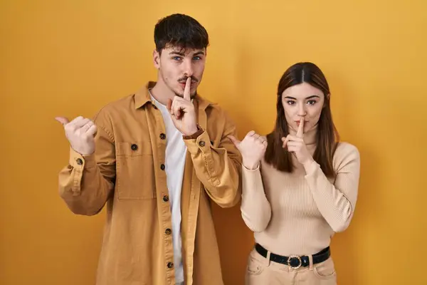 Young Hispanic Couple Standing Yellow Background Asking Quiet Finger Lips — Stock Photo, Image