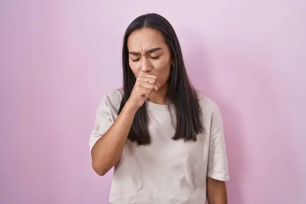 ピンクの背景に立つ若いヒスパニック系の女性は気分が悪く 風邪や気管支炎の症状として咳をします ヘルスケアの概念 — ストック写真