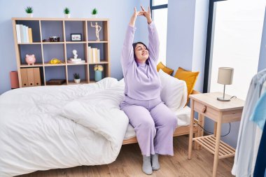 Young beautiful plus size woman waking up stretching arms at bedroom