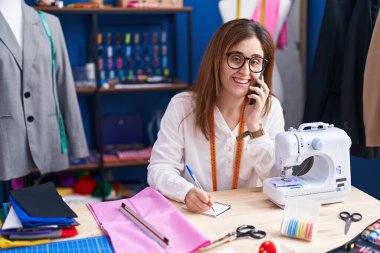 Dikiş atölyesinde akıllı telefon ile konuşan genç bir terzi.