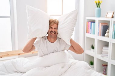 Genç sarışın adam yatak odasındaki gürültü için kulaklarını kapatıyor.