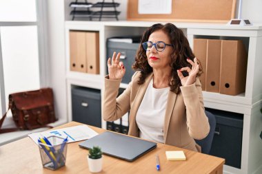 Middle age hispanic woman working with laptop doing yoga pose at the office