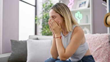 Evdeki kanepede oturan genç sarışın kadın stresli.
