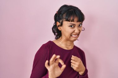 Pembe arka planda duran genç ve güzel bir kadın tiksindirici tepki verdiği için hoşnutsuz ve ürkek bir ifade takınıyor. Eller havada. 