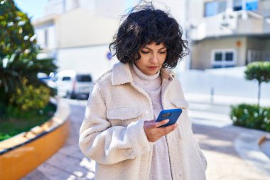 Genç, güzel, İspanyol bir kadın parkta akıllı telefon kullanıyor.
