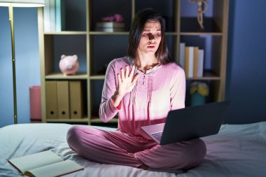 Yatakta dizüstü bilgisayar kullanan Latin kökenli genç bir kadın avuç içi hareketlerini durduruyor. Öfkeli ve hayal kırıklığı dolu ifadeler kullanıyor. 