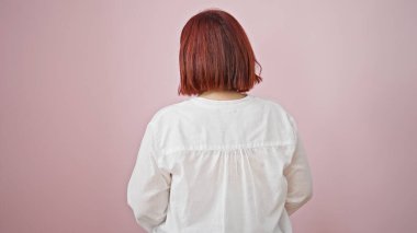 Soyutlanmış pembe arka planda geriye bakan orta yaşlı kadın.