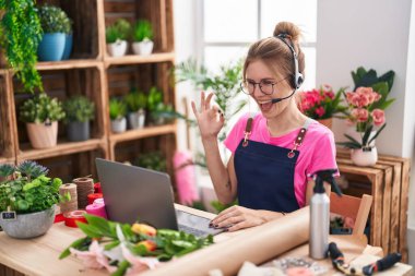 Çiçekçide çalışan sarışın, beyaz bir kadın video çekiyor. Parmaklarıyla imza atıyor, gülümsüyor. 