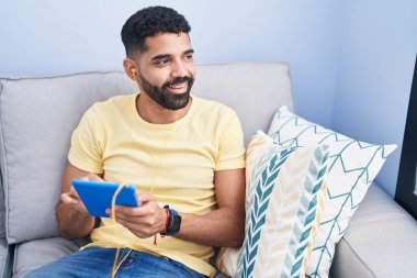 Genç Arap adam evdeki kanepede oturuyor.