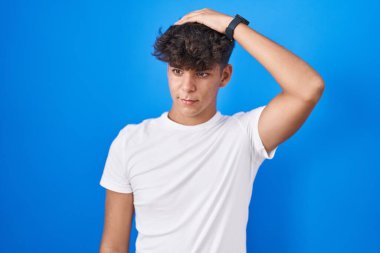 Mavi arka planda dikilen İspanyol genç kafası karışıyor ve soruyu merak ediyor. Şüpheyle kararsız, kafa kafaya düşünerek. Düşünceli kavram. 