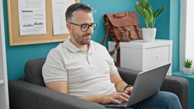 Ofiste çalışan beyaz saçlı bir iş adamı dizüstü bilgisayar kullanıyor.