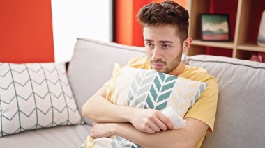 Genç İspanyol adam kanepede oturup evde yastığa sarılarak ağlıyor.