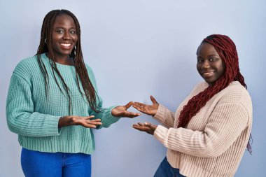 Mavi arka planda duran iki Afrikalı kadın gülümseyerek doğal bir şekilde içeri girmeye davet ediyor. 