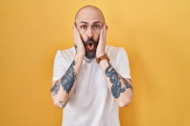 Sarı arka planda duran İspanyol dövmeli genç adam korkmuş ve şok olmuş, şaşırmış ve şaşırmış bir yüz ifadesi var. 