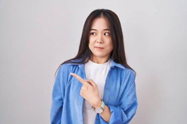 Beyaz arka planda duran genç Çinli kadın endişeli ve endişeli bir ifadeye işaret ediyor. 