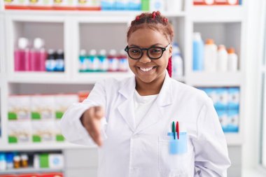 Afro-Amerikalı kadın eczacı gülümseyerek eczanede el sıkışıyor.