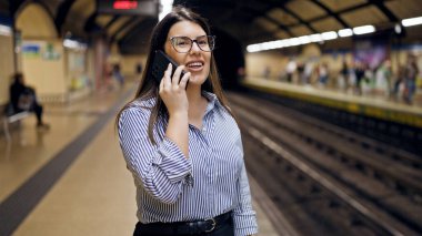 Madrid metro istasyonunda metroyu bekleyen genç ve güzel İspanyol kadın telefonda konuşuyor.