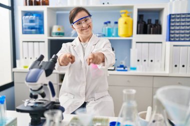 Down sendromlu İspanyol kız bilim adamı laboratuarında çalışıyor. Seni ve kamerayı işaret ediyor. 