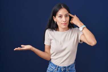 Mavi arka planda dikilen genç İspanyol kadının kafası karışmış ve avuç içi açık bir şekilde fotokopi alanı göstermesi ve alnını işaret etmesi canını sıkmış. Bunu bir düşün.. 