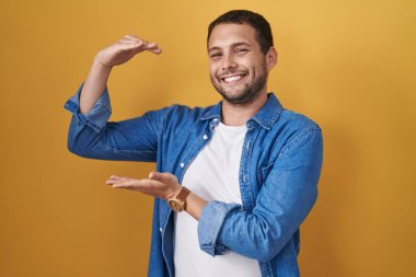 Sarı arka planda duran İspanyol adam. Elleriyle büyük ve büyük bir işaret gösteriyor. Ölçü sembolü. Kameraya bakıp gülümsüyor. ölçüm kavramı. 