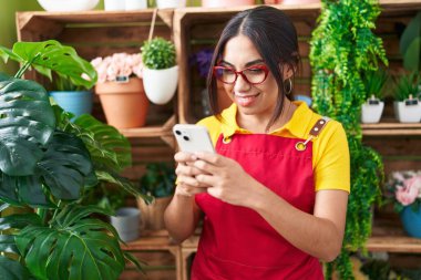 Çiçekçide akıllı telefon kullanarak gülümseyen güzel bir Arap kadın.