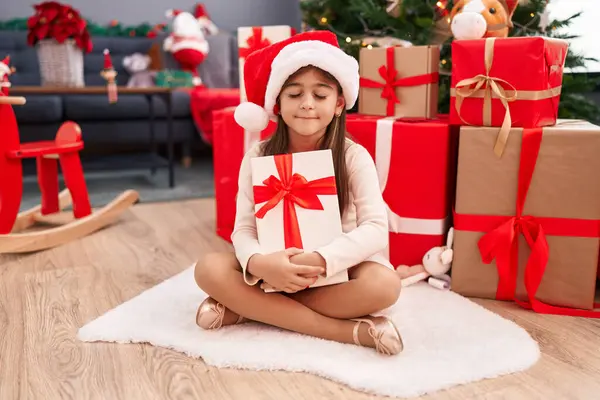 Adorable Hispanic Girl Hugging Christmas Gift Sitting Floor Home — Stock Photo, Image