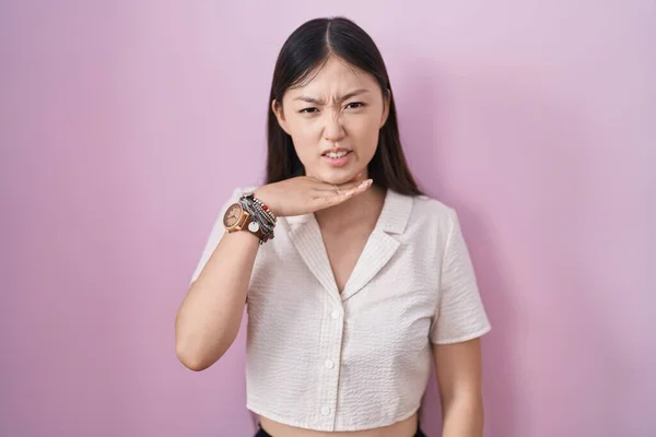 ピンクの背景の上に立っている中国の若い女性は ナイフとして手で喉を切って 激しい暴力で侵略を脅かします — ストック写真
