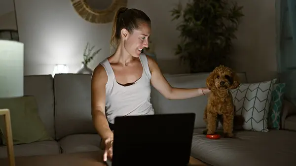 Молодая Белая Женщина Собакой Улыбается Используя Ноутбук Сидя Дома Диване — стоковое фото
